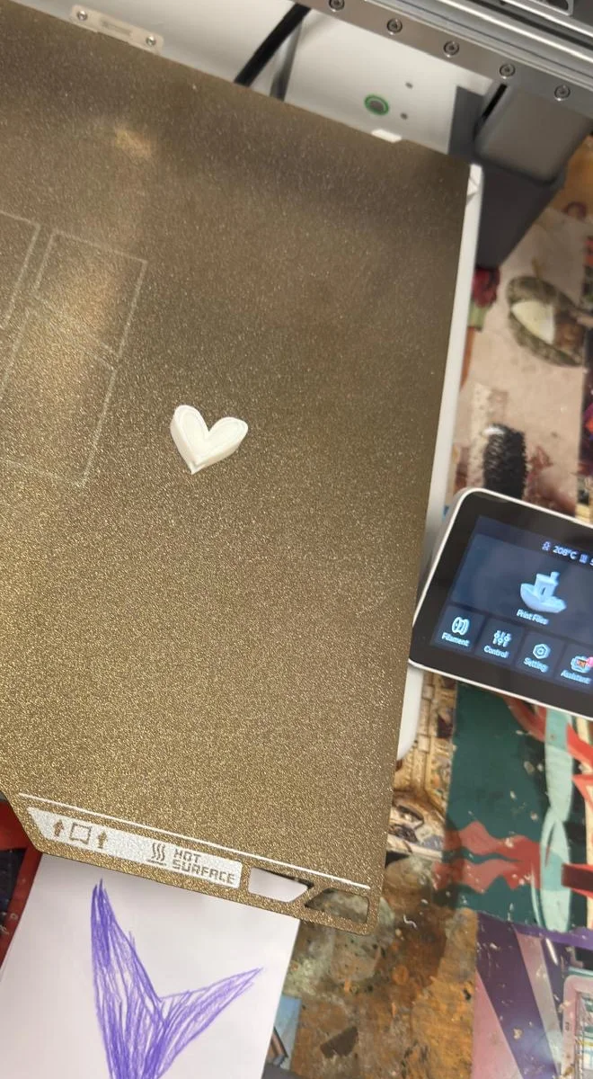 Il cuore appena stampato sul piatto della stampante 3D, con il disegno originale appoggiato davanti.